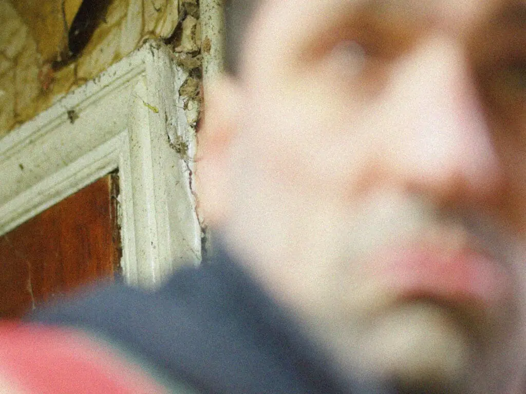 Shot of a Tommy Cooper impersonator out of focus in a rundown kitchen.